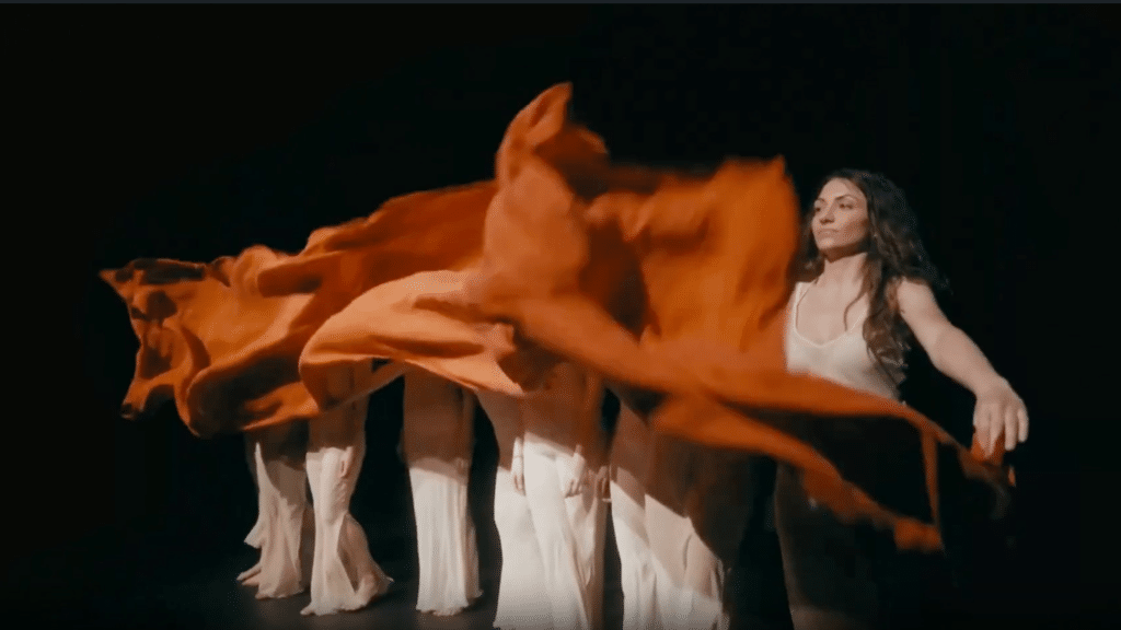 Il team WIDE durante una performance artistica, con donne in abiti trasparenti che sventolano drappi rossi, rappresentando creatività e innovazione. Scopri artisti e creativi che lavorano con passione per creare esperienze ispiranti e trasformative.